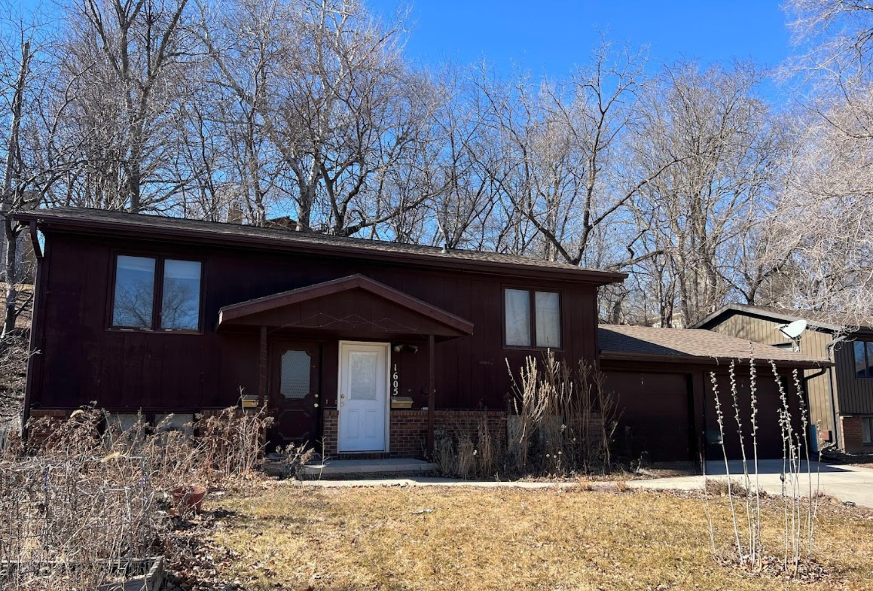 A large brown house with a porch and trees in the background.