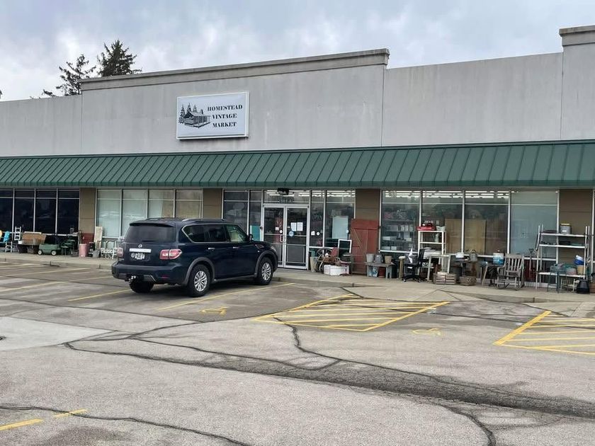 Strip mall storefront with a green awning, parked SUV, and outdoor tables on a cloudy day