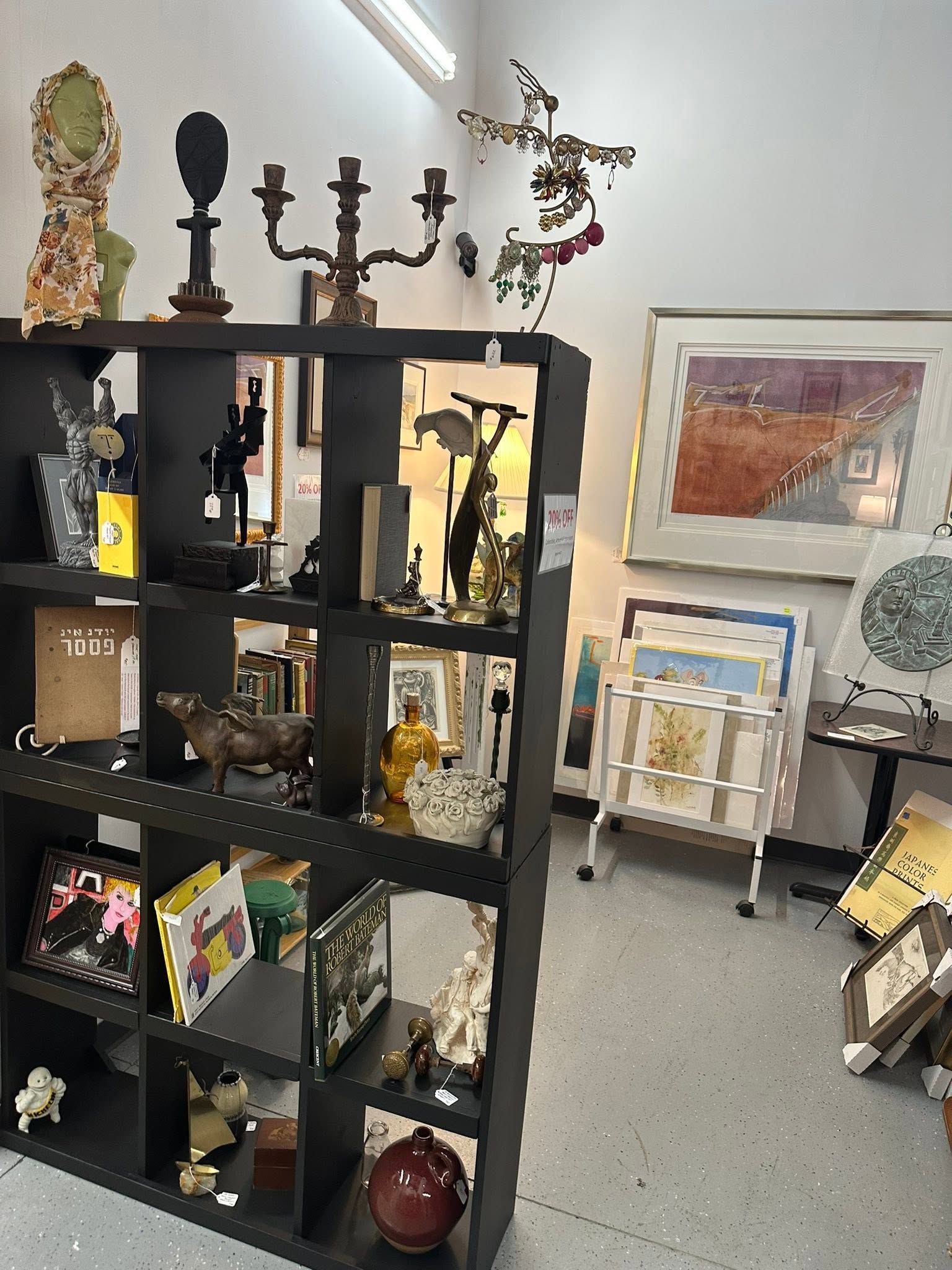 Black shelving unit with assorted art objects and decor in a bright gallery or shop interior.