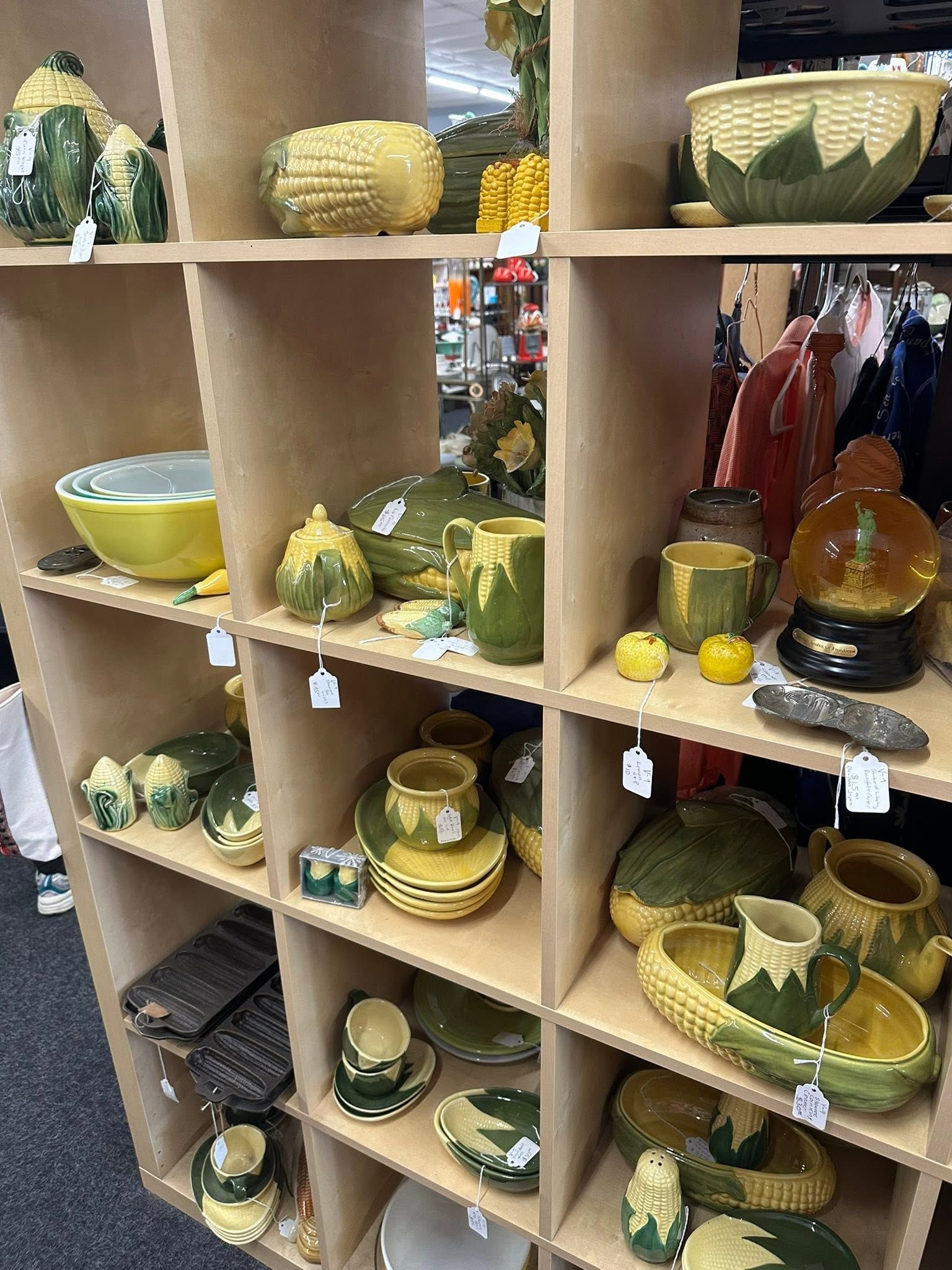 Wooden cubby shelves filled with green and yellow decorative bowls, cups, and pitchers in a store.