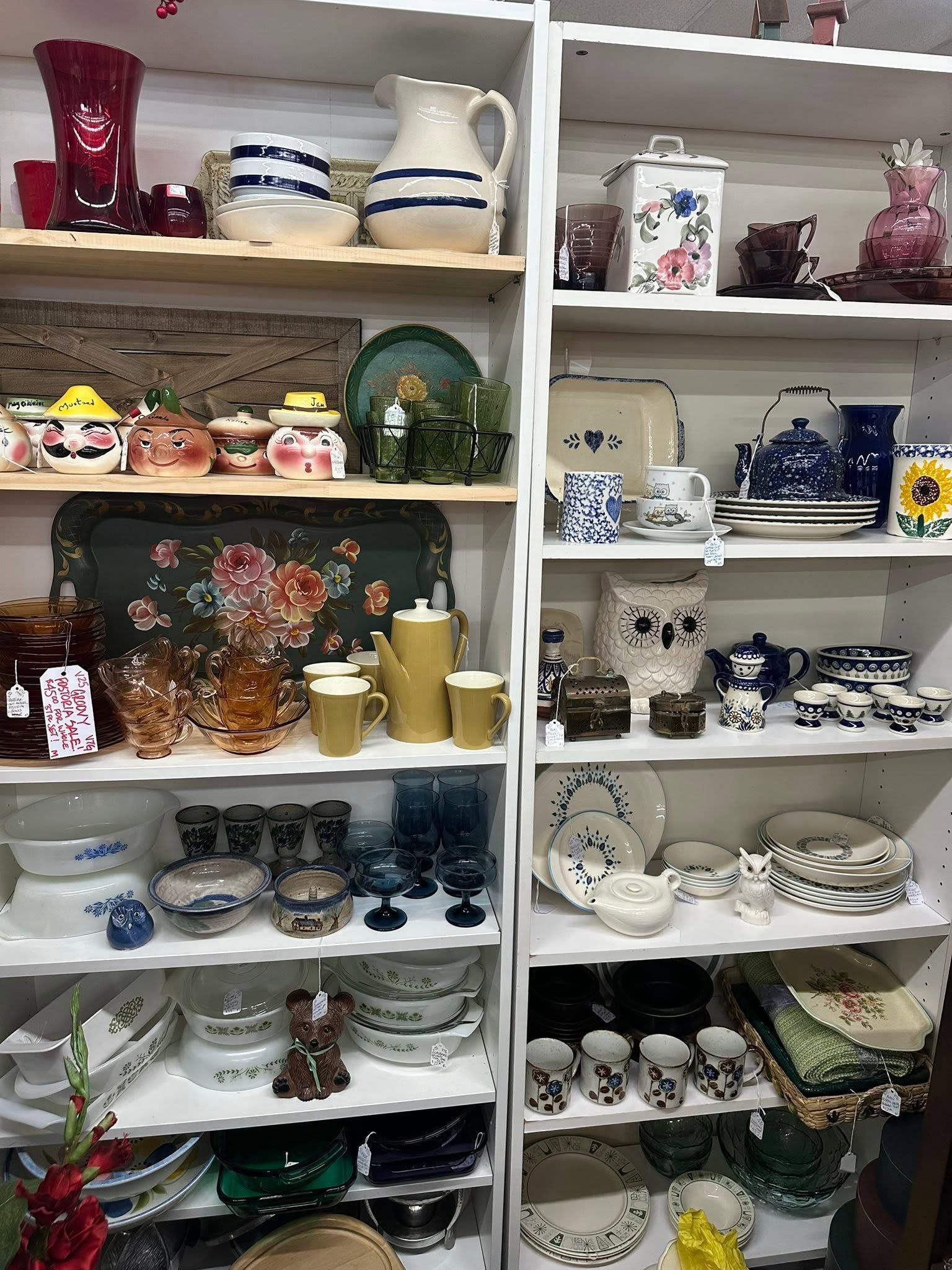 Shelves packed with assorted vintage dishes, teapots, glassware, and decorative ceramics in a shop display