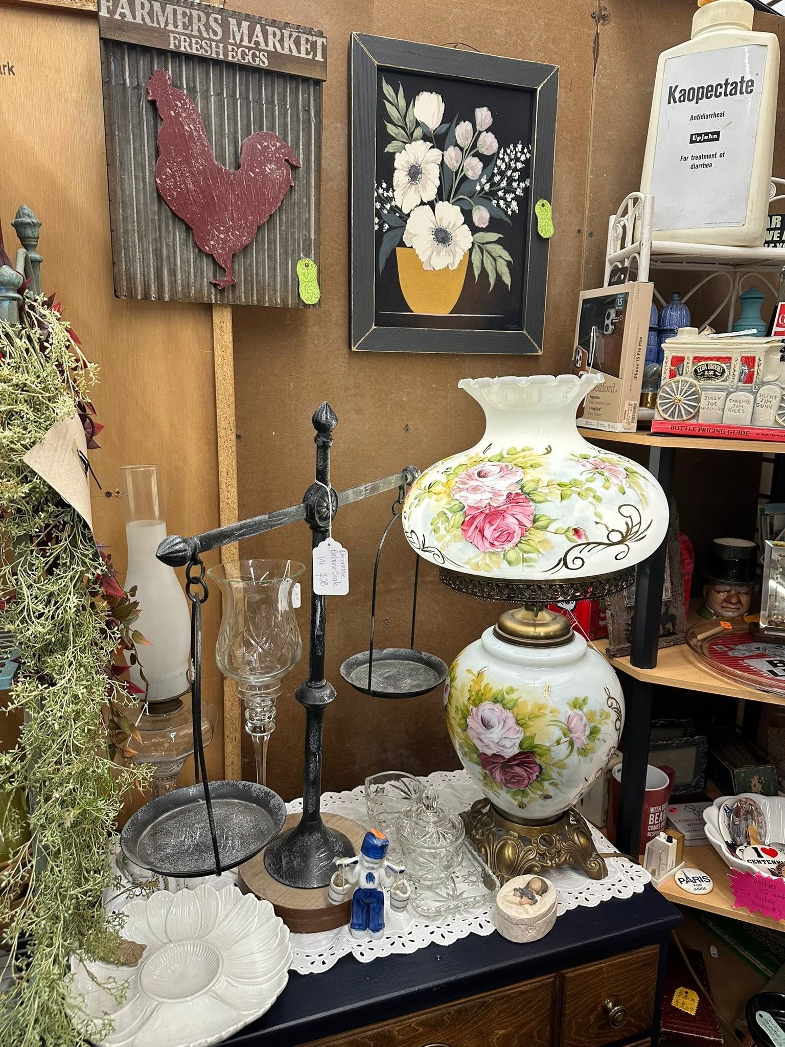 Antique booth display with floral vases, framed art, lamps, and decorative collectibles on shelves and tables