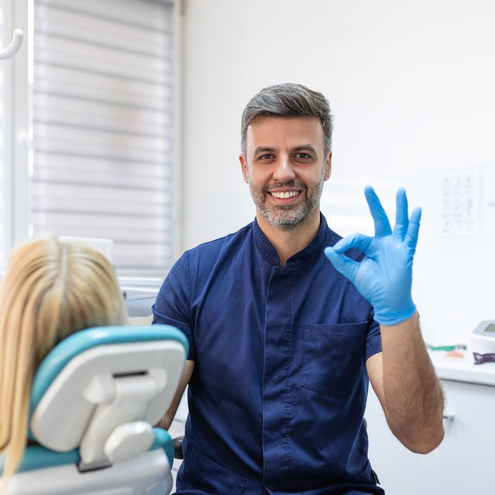 Un dentista le está dando una señal de aprobación a un paciente en una silla dental.