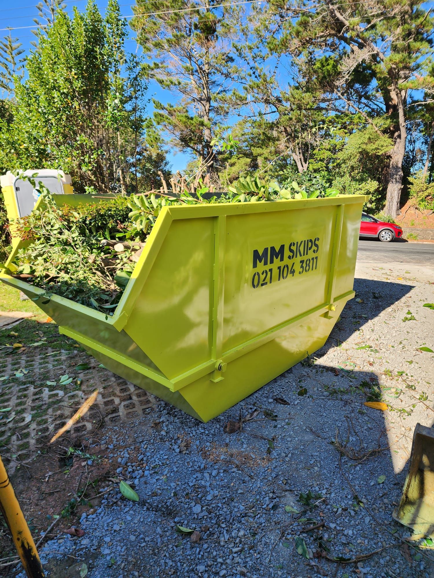 Green metal dumpster beside a white barrel against a corrugated wall