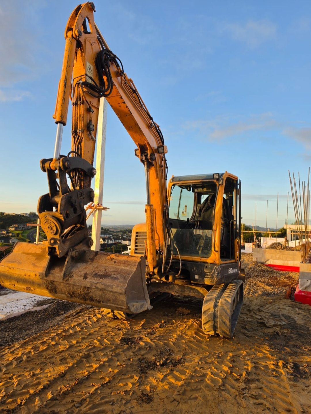 Orange excavator digging in a muddy field under a cloudy sky