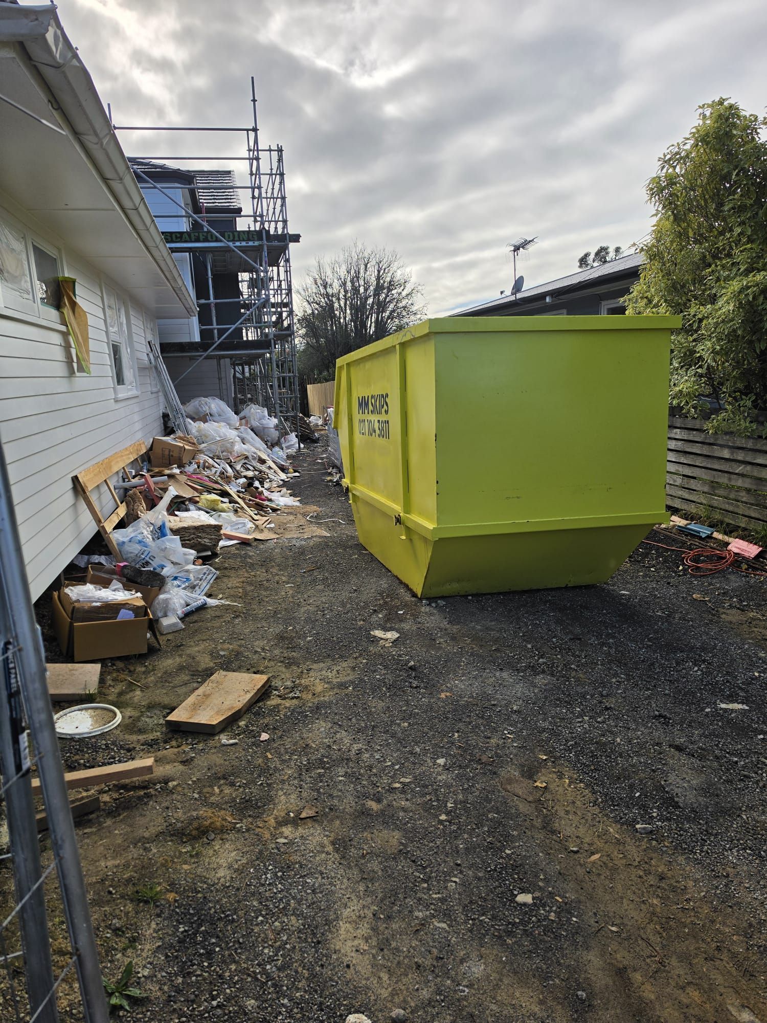 Yellow dumpster beside a building with trash piles along a narrow gravel alley