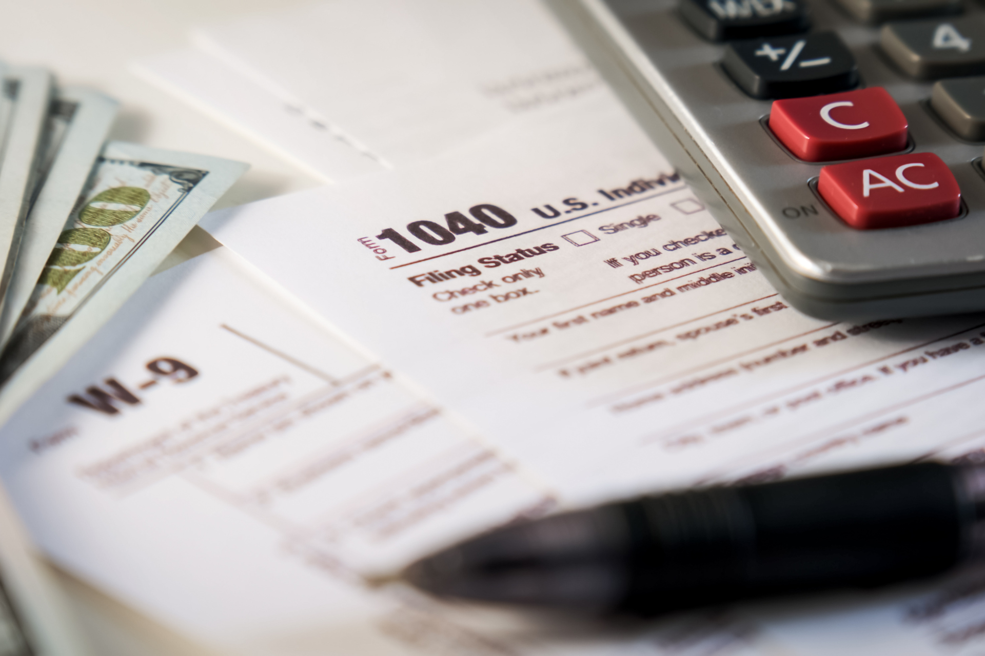 1040 tax form with calculator, pen, and dollar bills on a desk