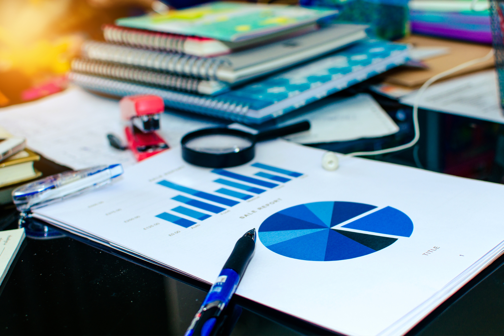 Desk with financial charts, pen, magnifying glass, and stacked notebooks in a workspace