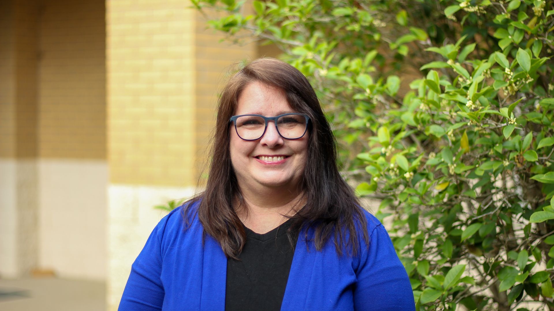 A woman wearing glasses is smiling in front of a church.