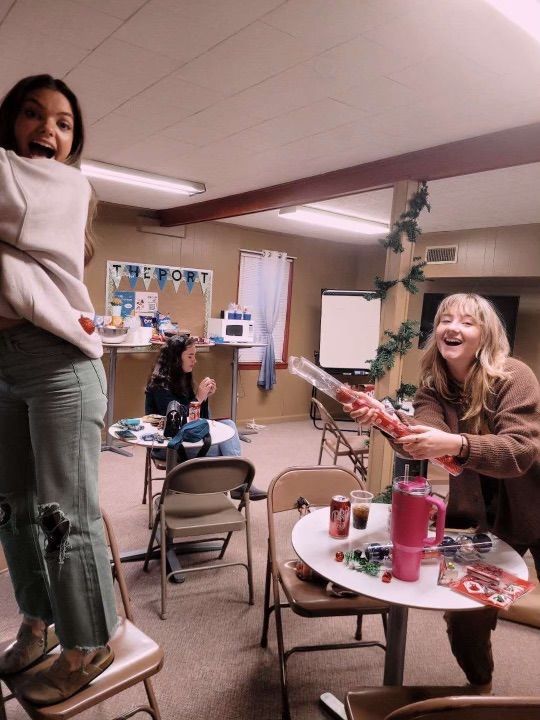 Two girls are standing in a room with tables and chairs.