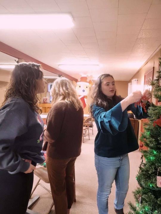Three women are decorating a christmas tree in a room.