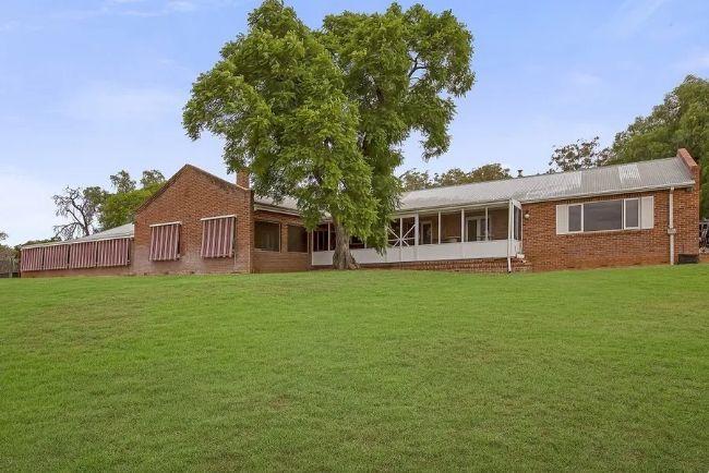A large brick house sits in the middle of a lush green field.