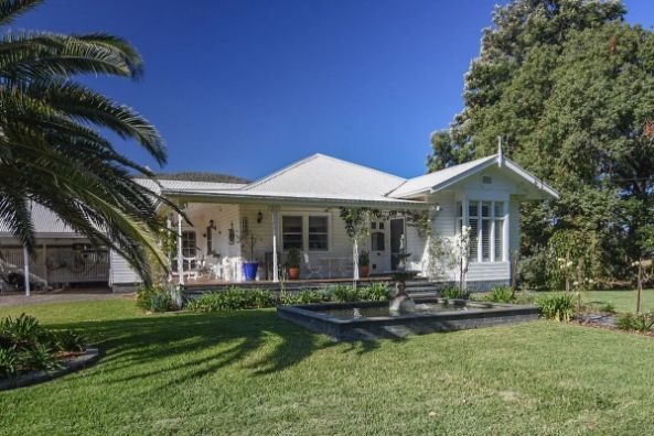 A white house with a large lawn and palm trees in front of it.