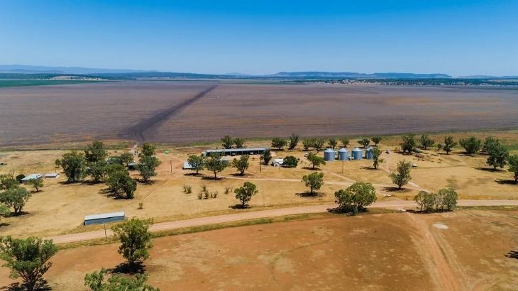 An aerial view of a large dry field with trees and buildings.