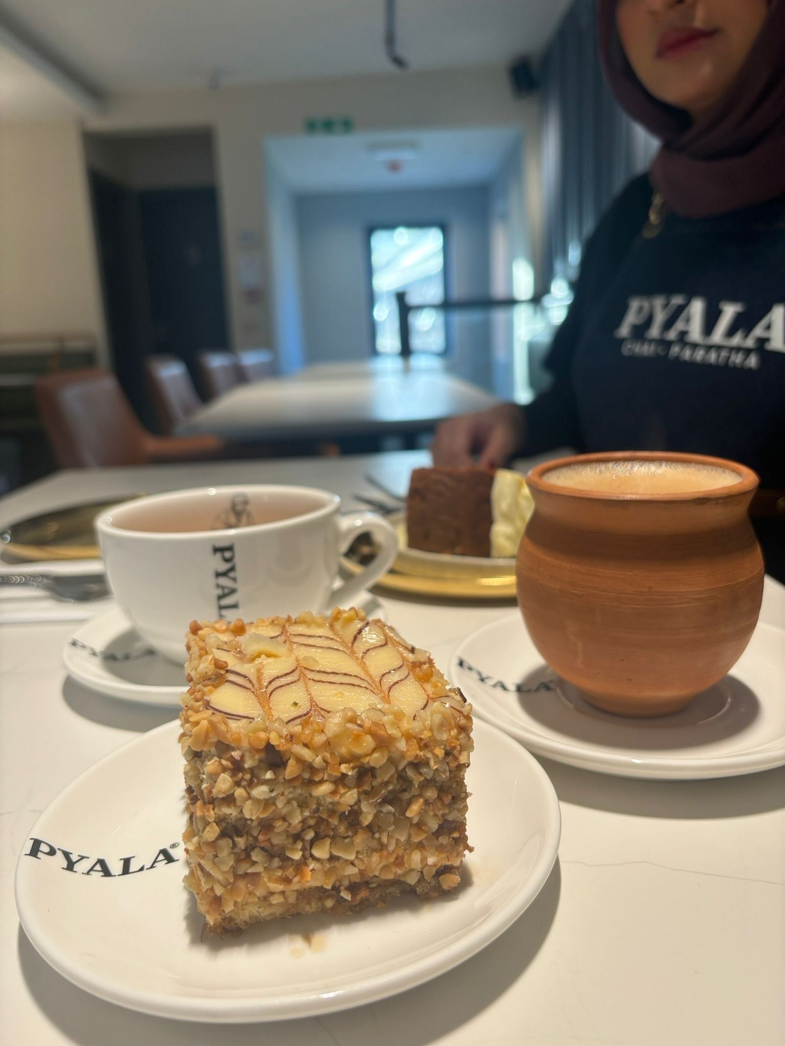 A dessert with a drink on a table in a cafe, with a person in the background.