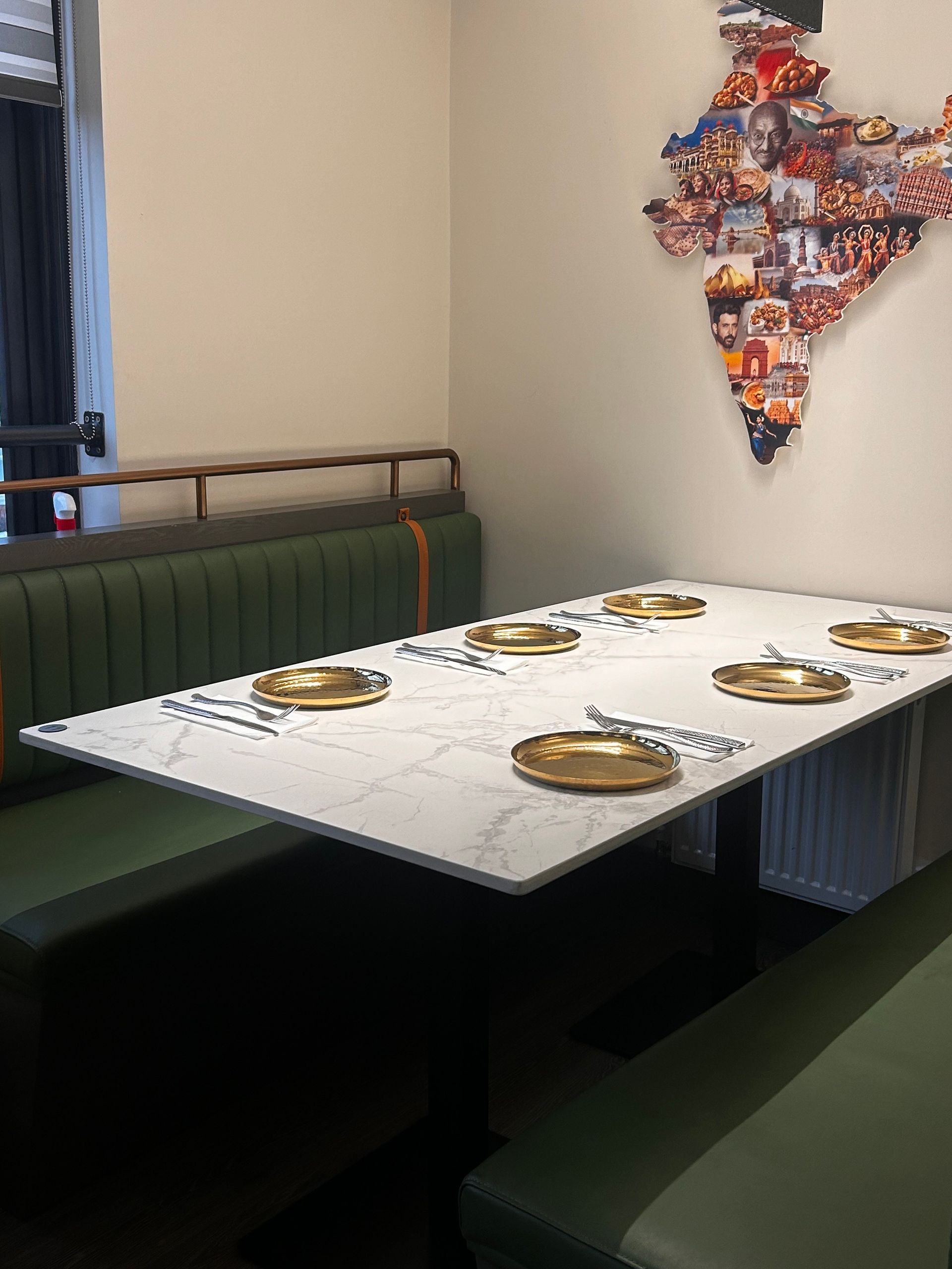 Restaurant booth with green seats, marble-like table, brass plates with map art on the wall.