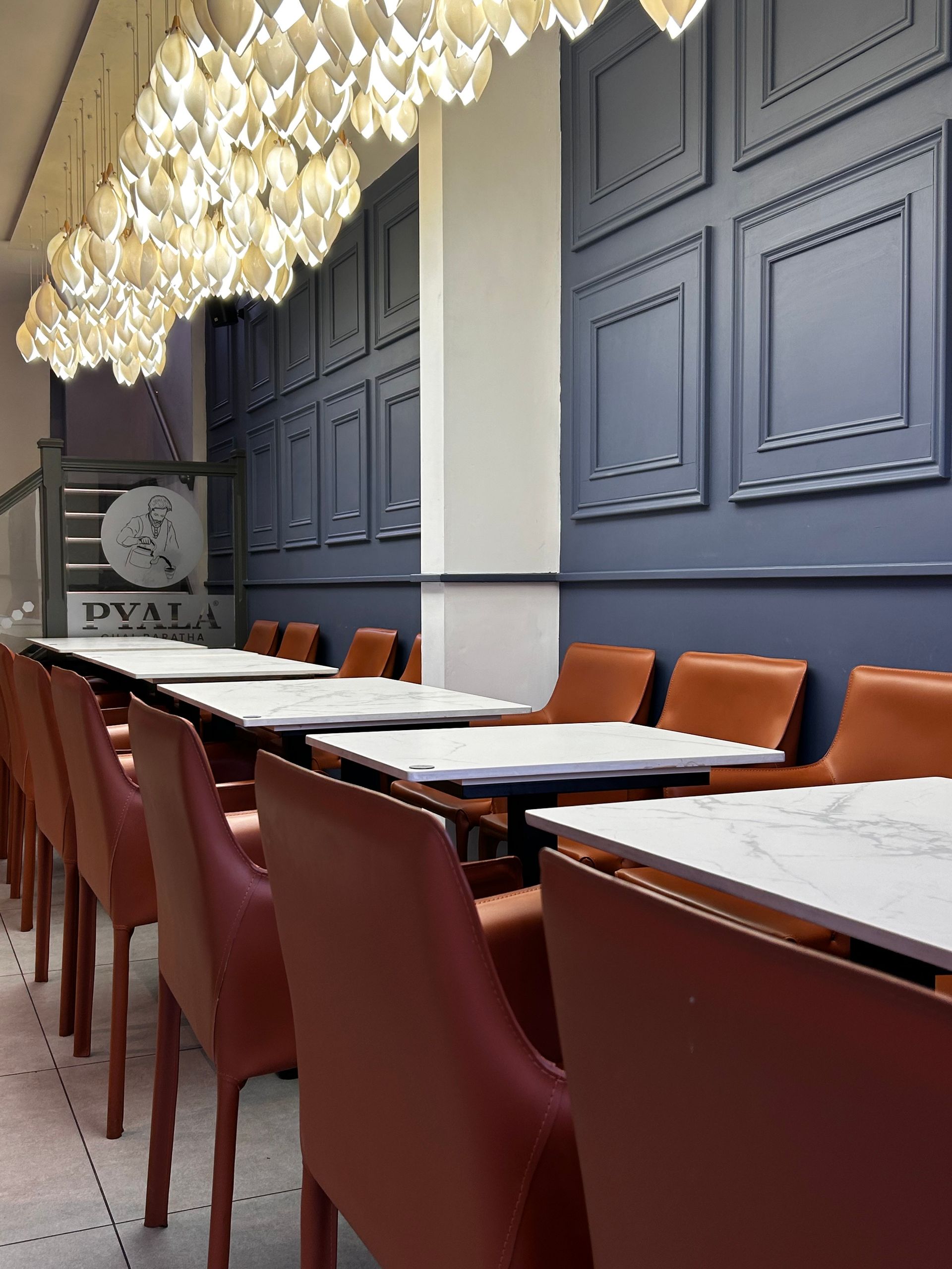 Restaurant interior with tables, chairs, and ornate ceiling lights against a blue paneled wall.