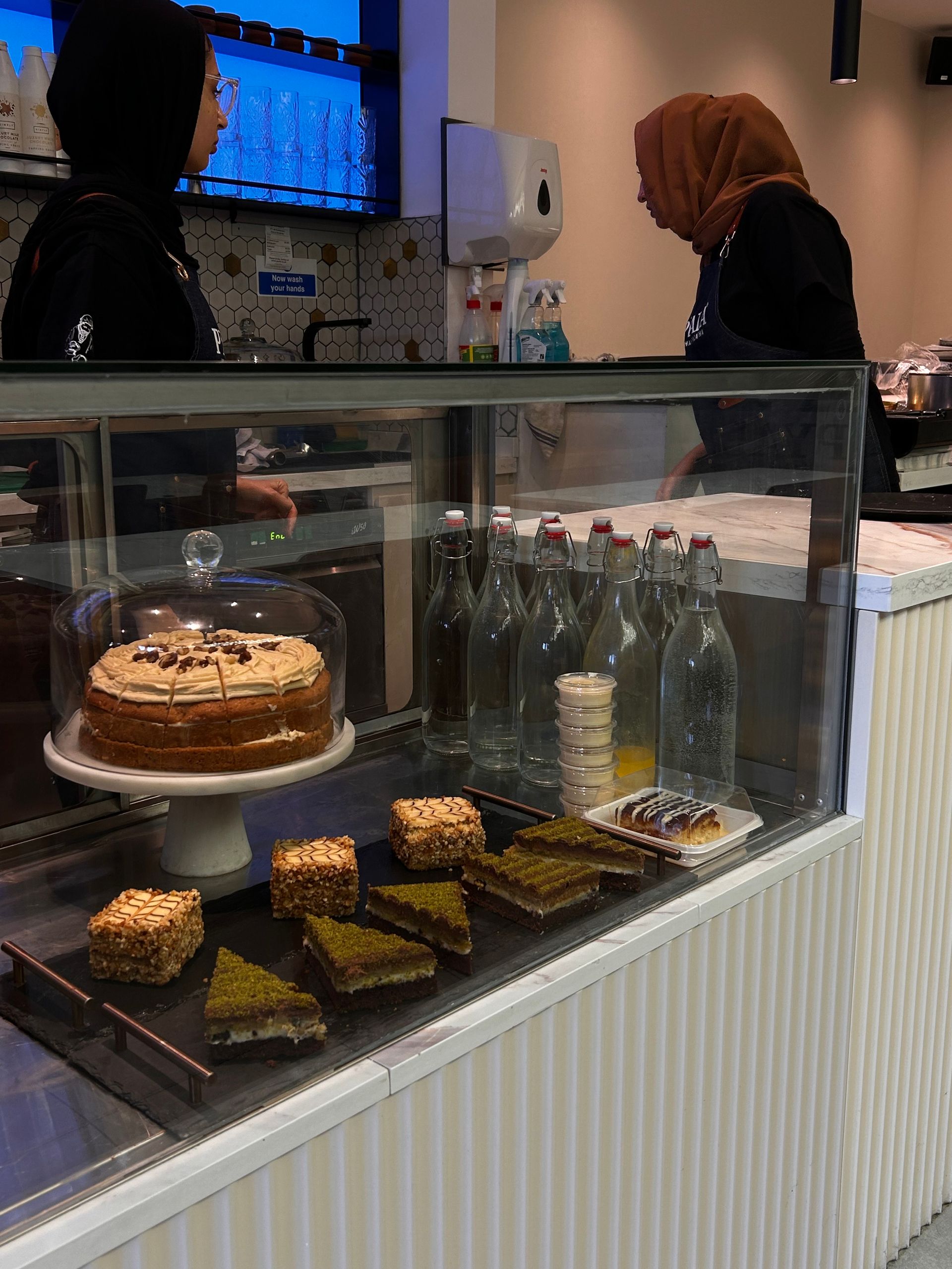 A pastry display case in a cafe with a cake and baked goods. Two women behind the counter.