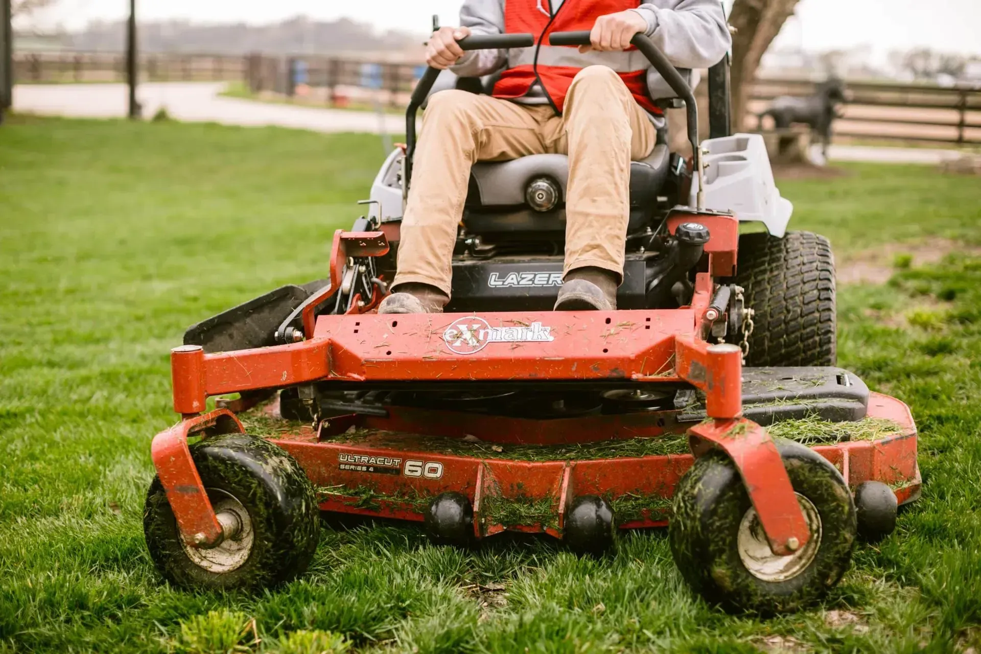 Person on a red zero-turn lawnmower cutting grass on a green lawn.
