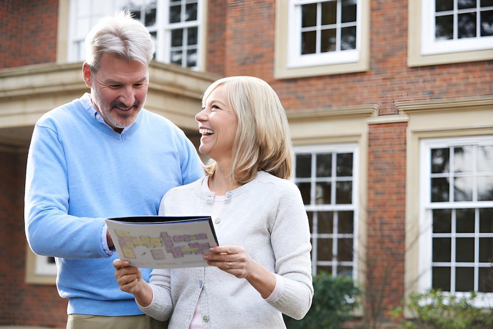 A Man And A Woman Are Standing In Front Of A Brick House Looking At A Map — Romy Sidhu Ray White Weir Views In Melton, VIC
