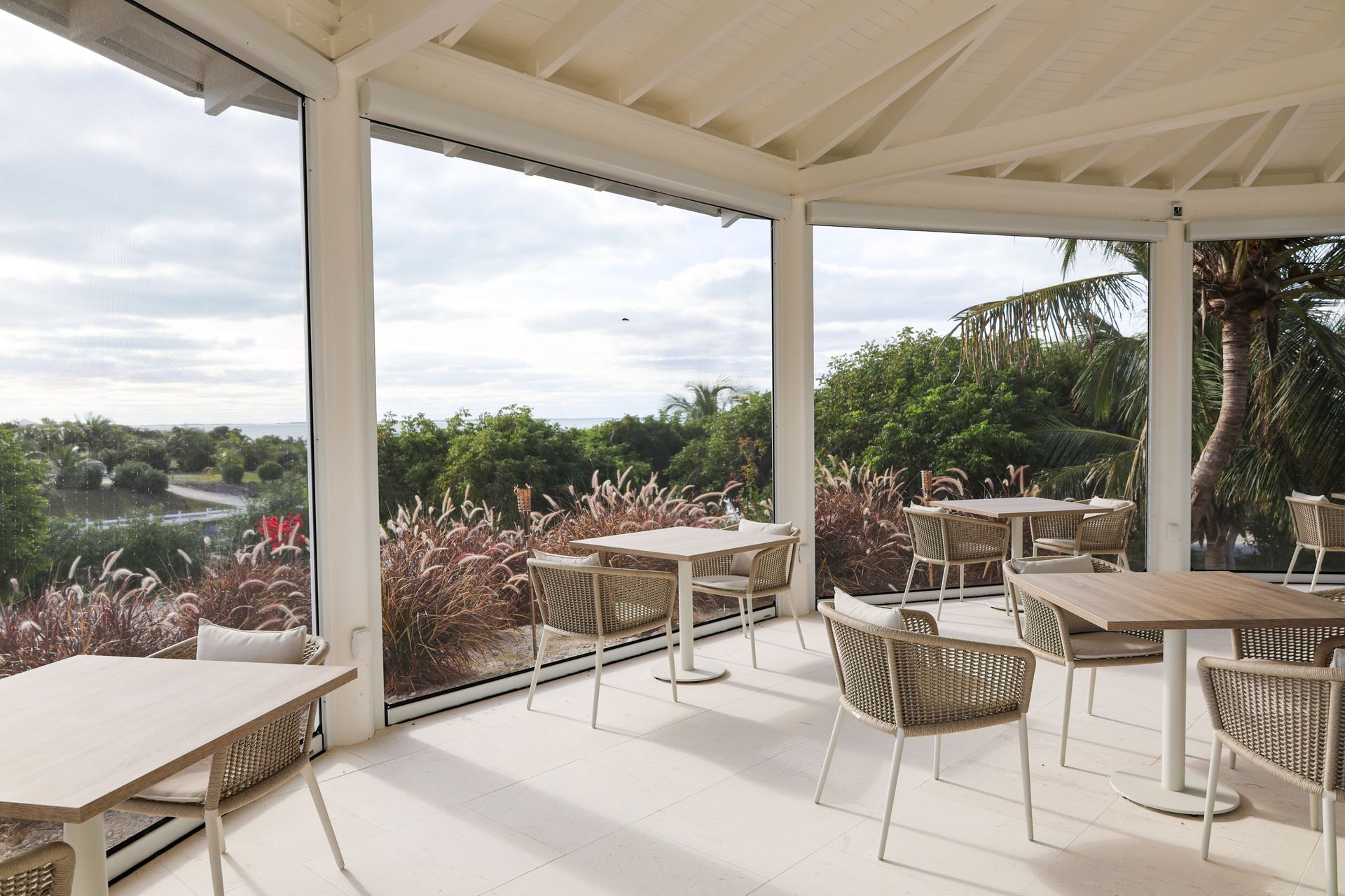 Open-air café patio with tables and chairs overlooking trees and a cloudy sky