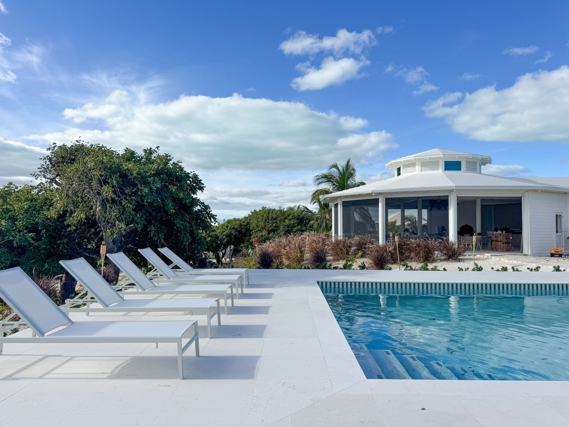 White lounge chairs by a blue pool beside a modern white house under a partly cloudy sky