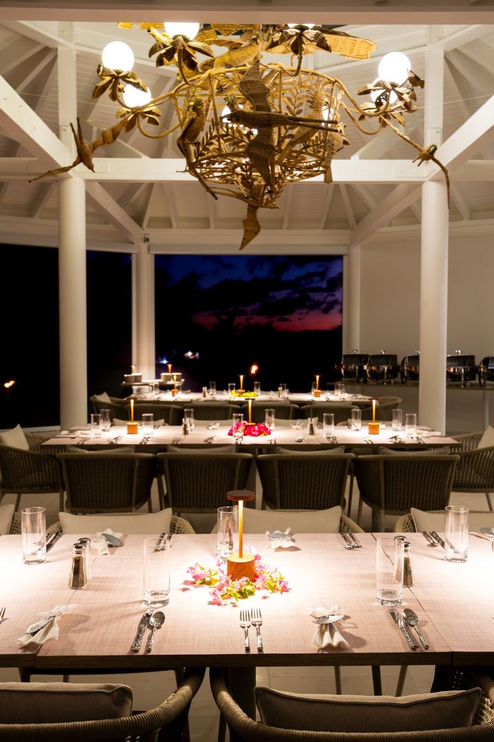 Elegant banquet hall with white tables, gold chandelier, and a sunset view through large windows.