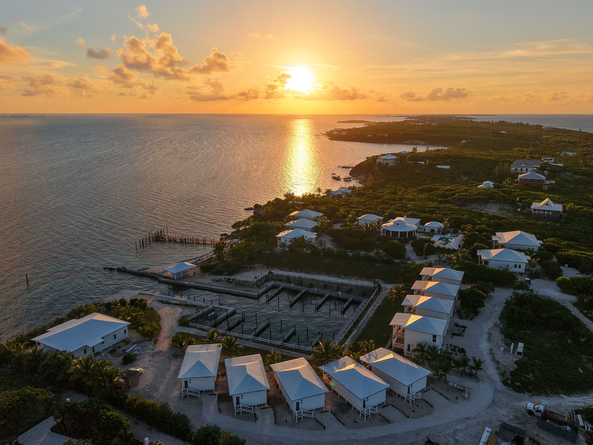 Sunset over a coastal resort with boats, white villas, and calm water reflecting the golden sky