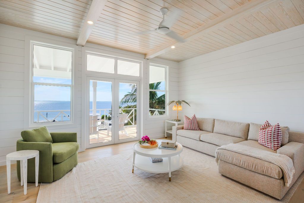 Bright coastal living room with white walls, beige sofa, green chair, and ocean view through large windows