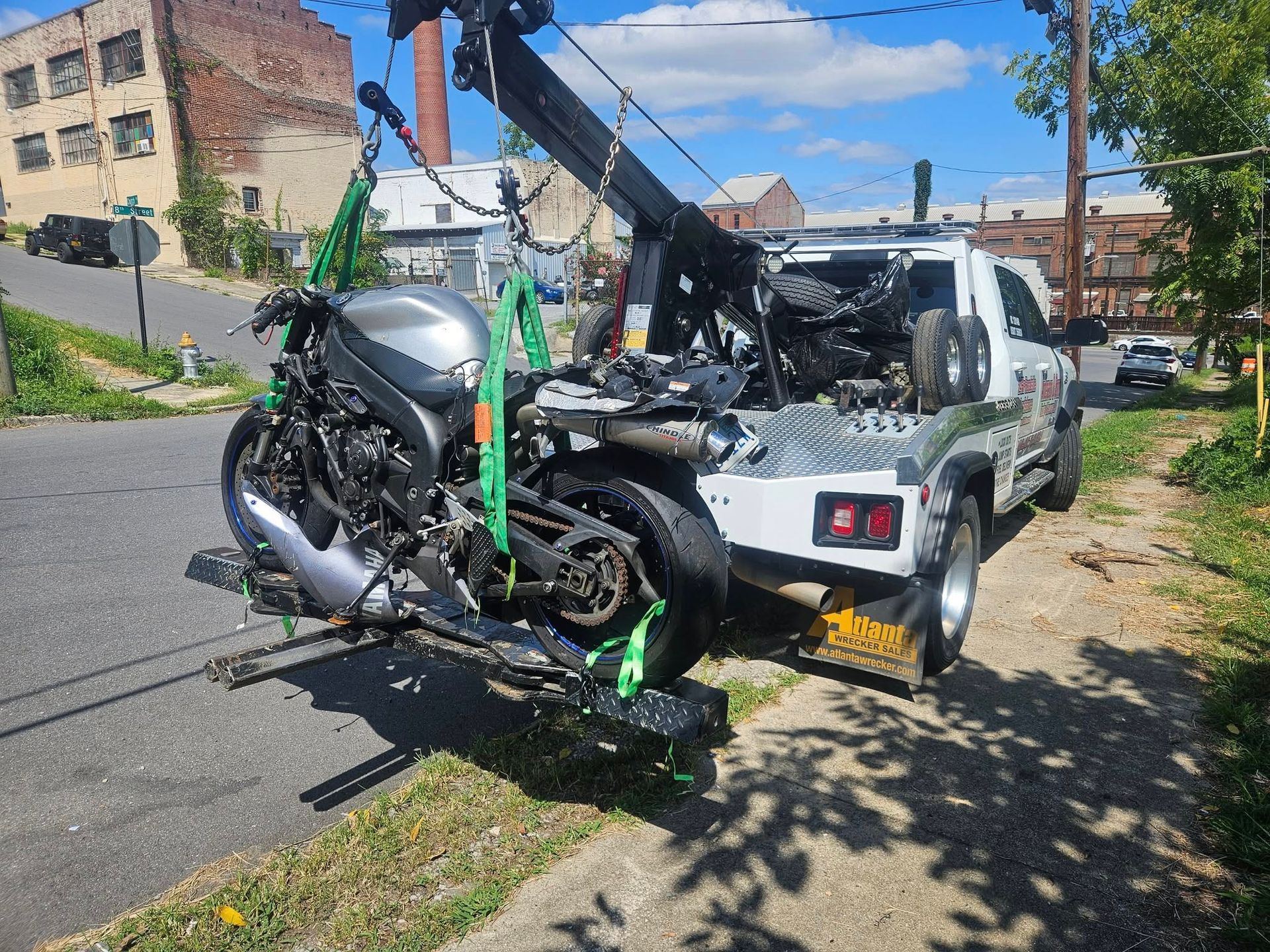 Motorcycle strapped to a tow truck on a city street, with damaged parts visible.