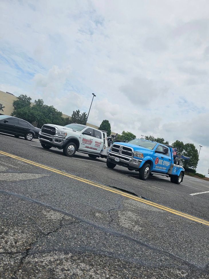 Two pickup trucks with trailers parked in a lot under cloudy skies, one blue and one silver.