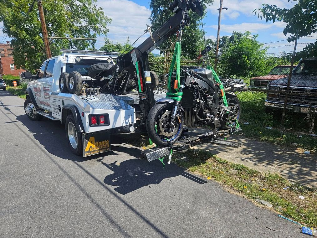 Tow truck carrying a damaged green motorcycle on a city street under a blue sky