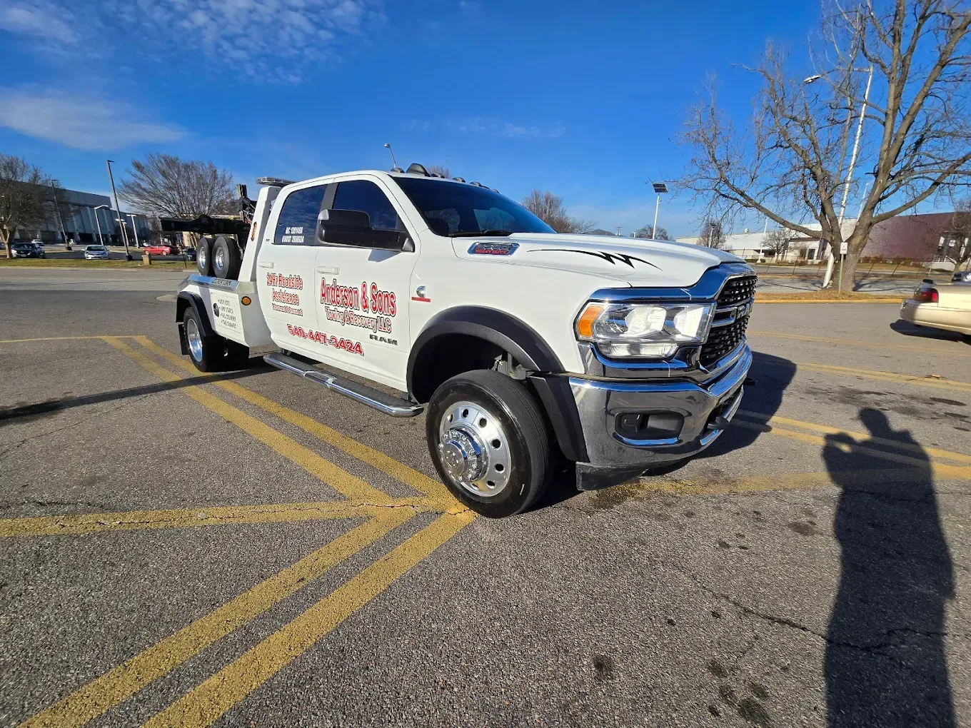 White utility truck parked in a lot on a sunny day, with trees and blue sky in the background.