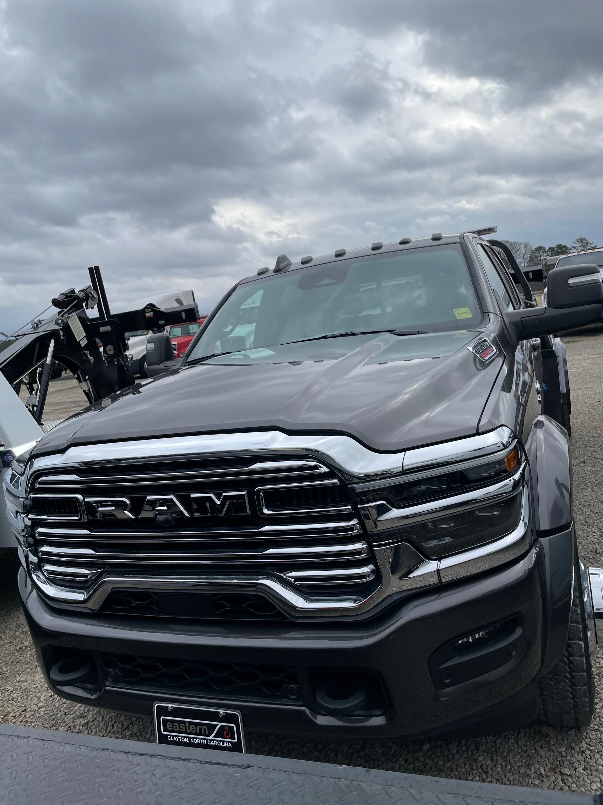 Damaged dark gray pickup truck in a lot under cloudy skies, front grille crushed and windshield cracked