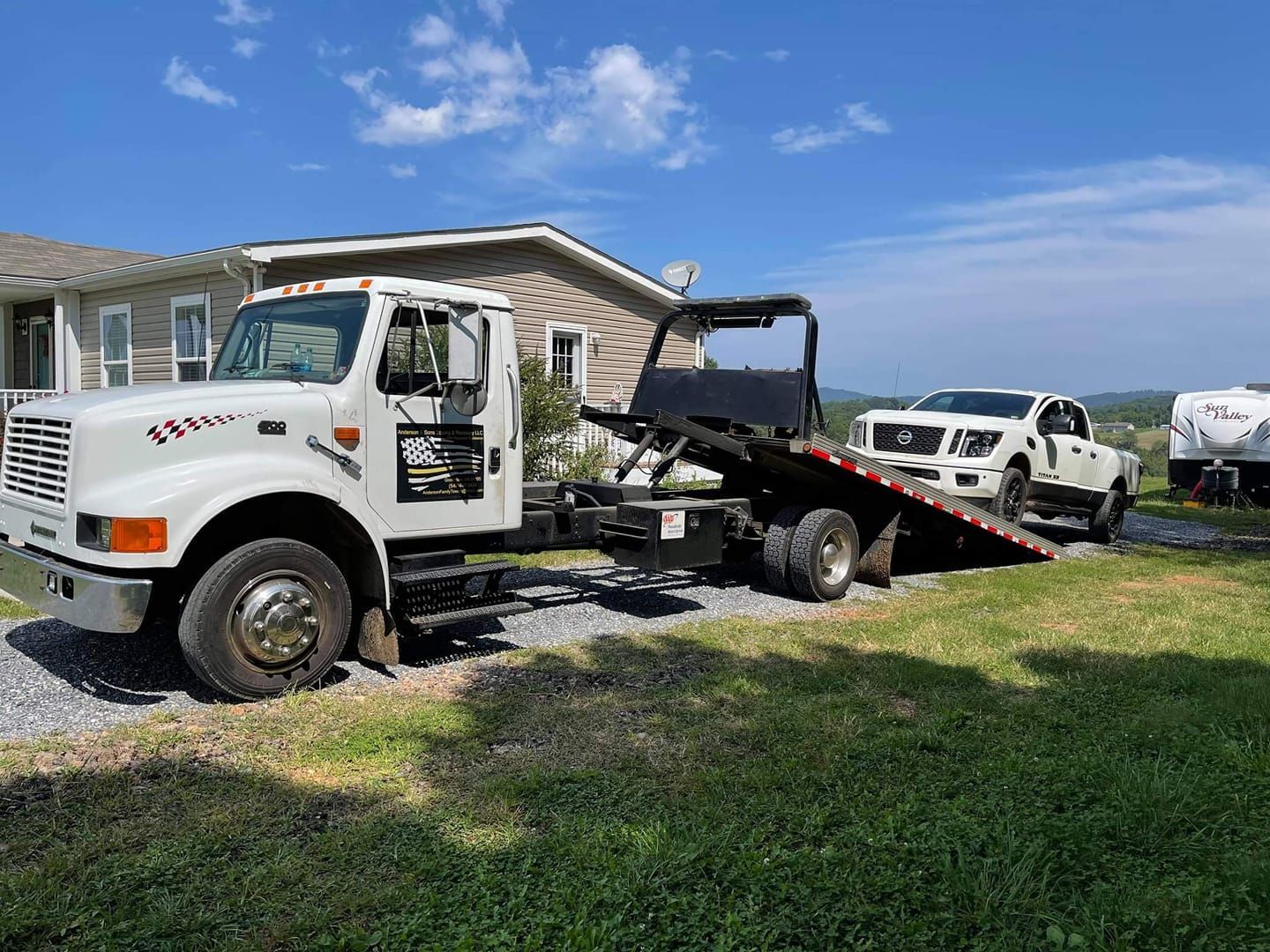 White tow truck loading a damaged pickup onto a flatbed beside a house