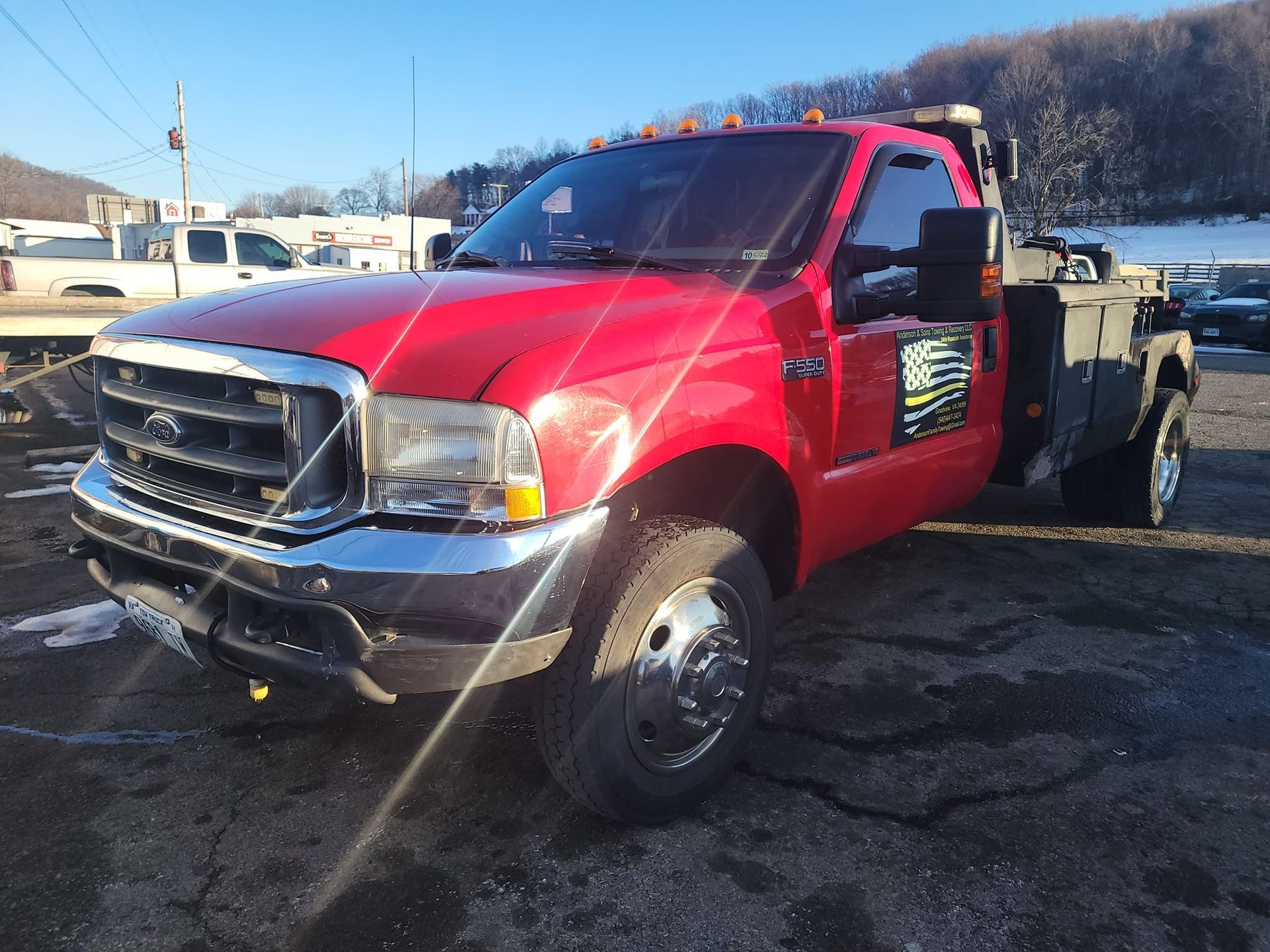 Red tow truck with damaged front end parked on a snowy lot in bright sunlight