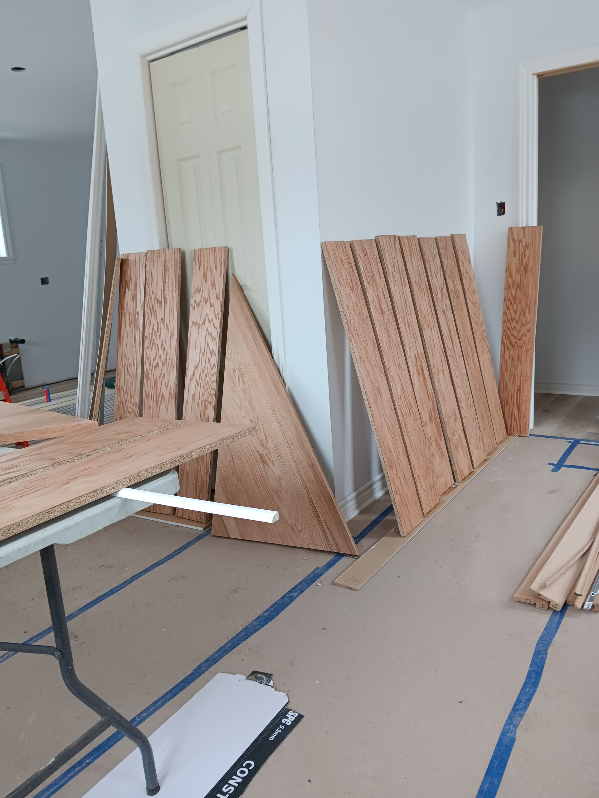 Planches de bois et porte appuyées contre un mur pendant la construction ; table de travail et porte ouverte visibles.