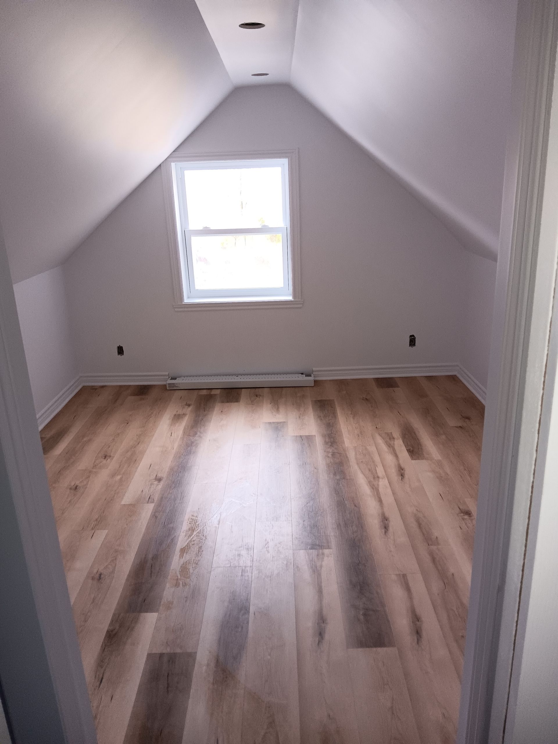 Un grenier vide avec du parquet et une fenêtre.