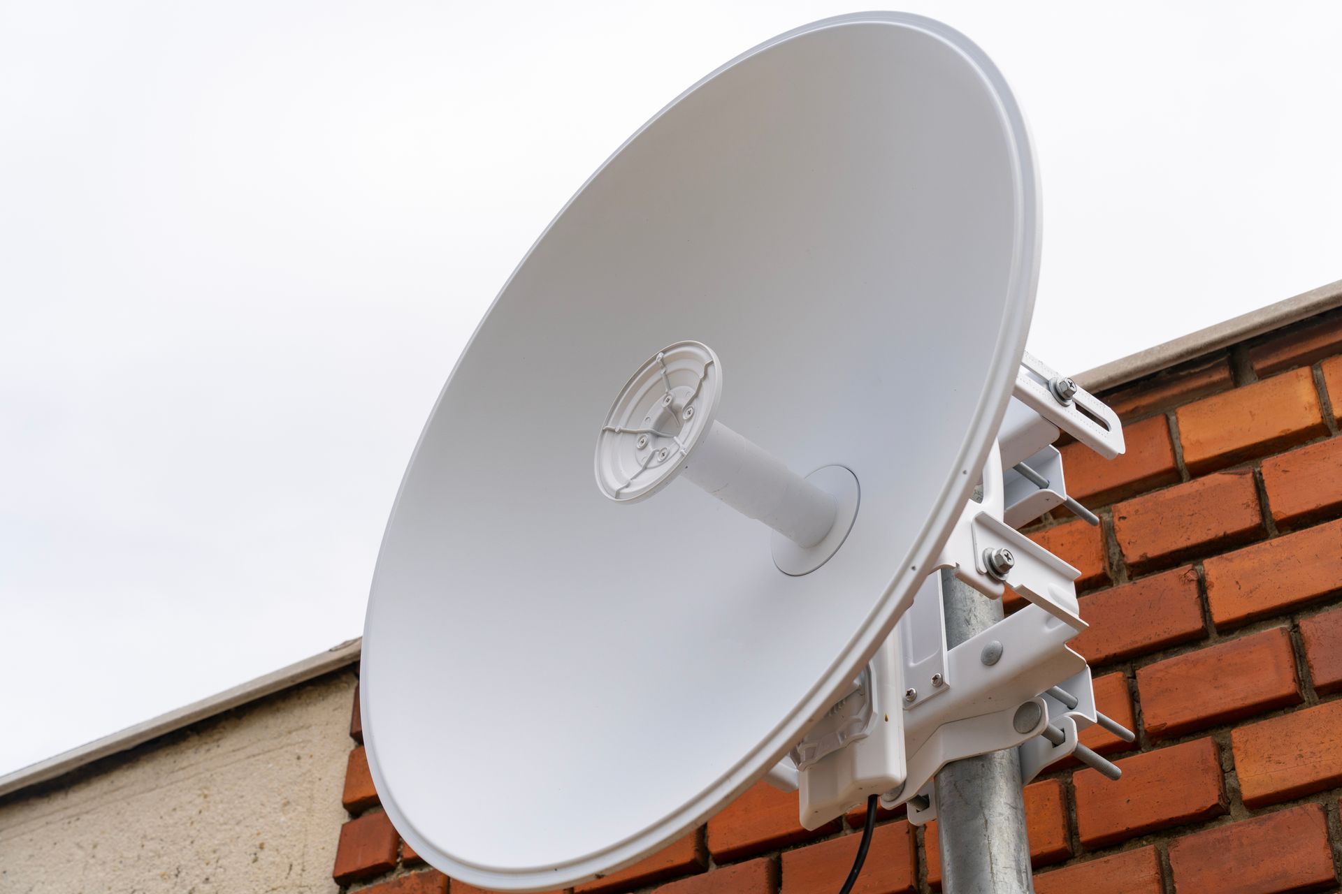 White satellite dish mounted on a brick wall outdoors