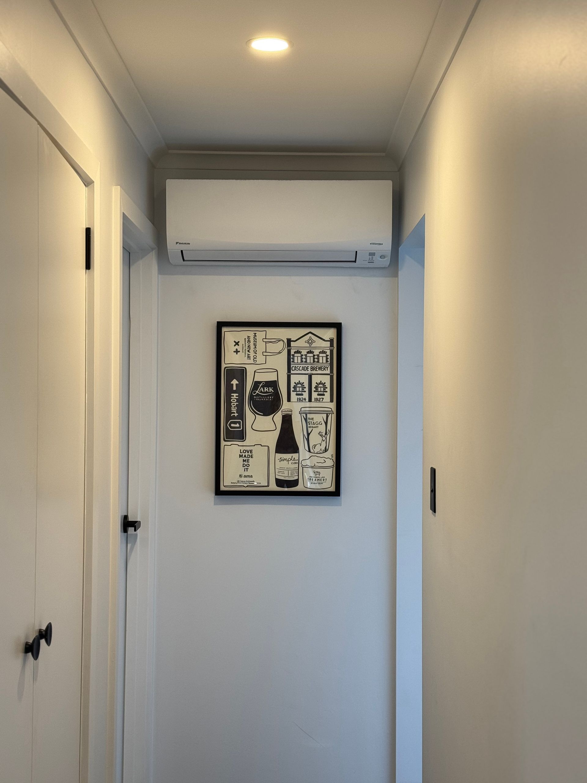 Narrow white hallway with a wall-mounted air conditioner and framed artwork at the end.