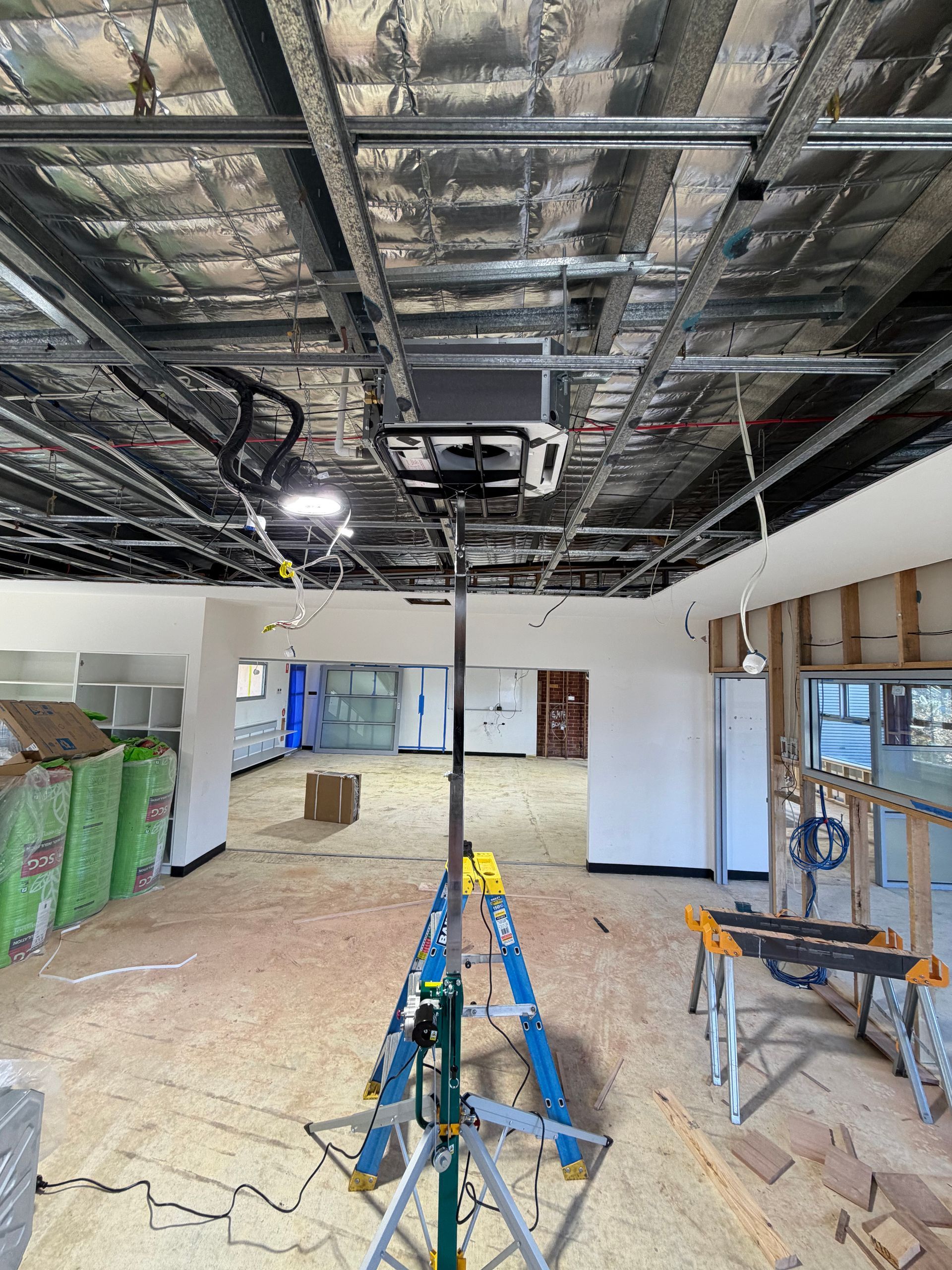 Renovation site with exposed ceiling, ladders, tools, and construction materials in an empty room.