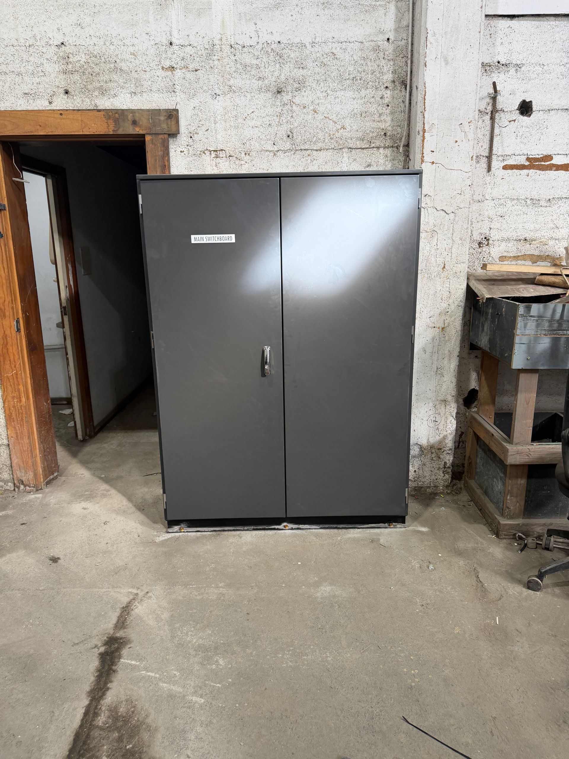 Dark gray metal cabinet in a concrete basement near a doorway and a workbench.
