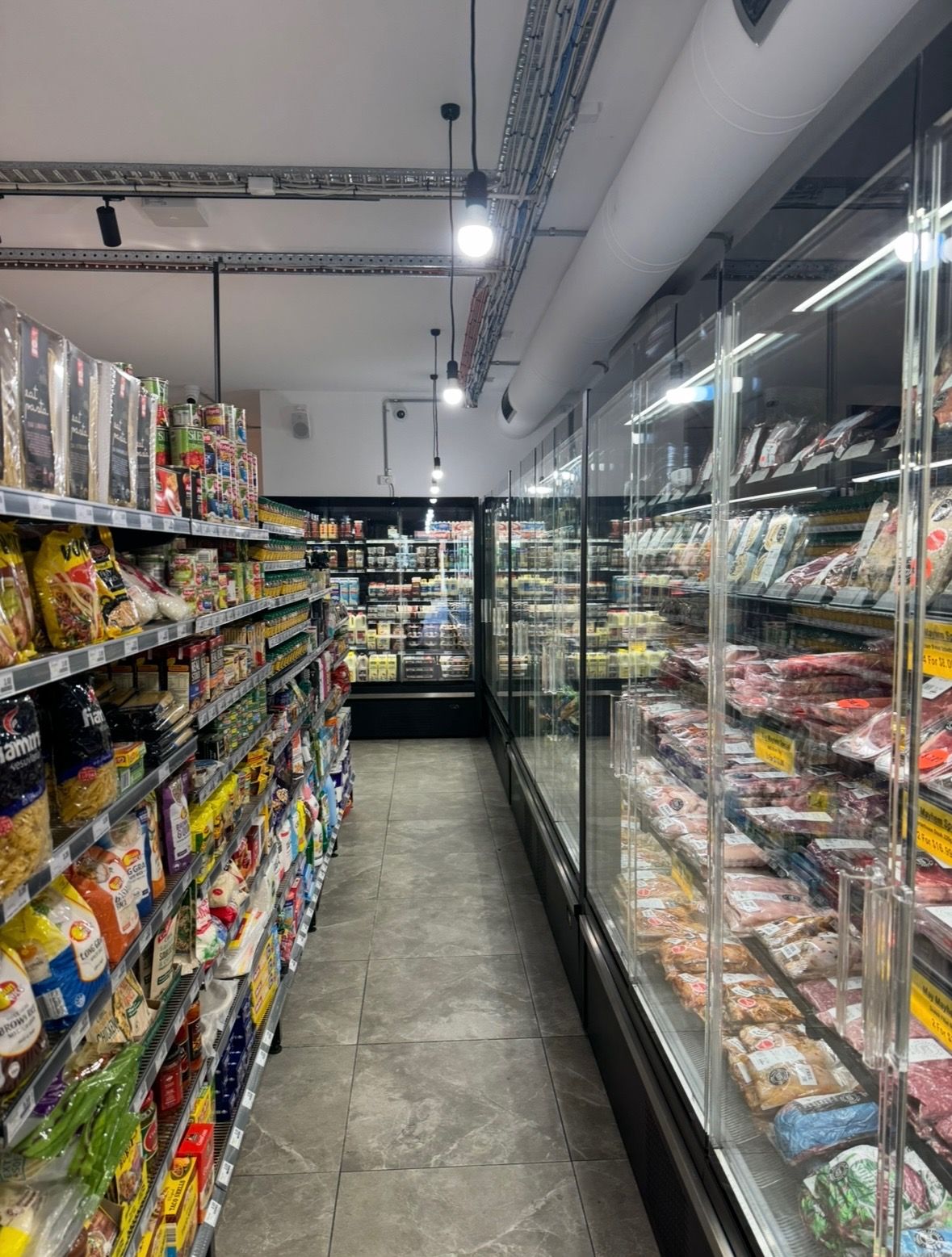 Narrow grocery aisle with shelves of packaged snacks and a glass refrigerated display on the right.