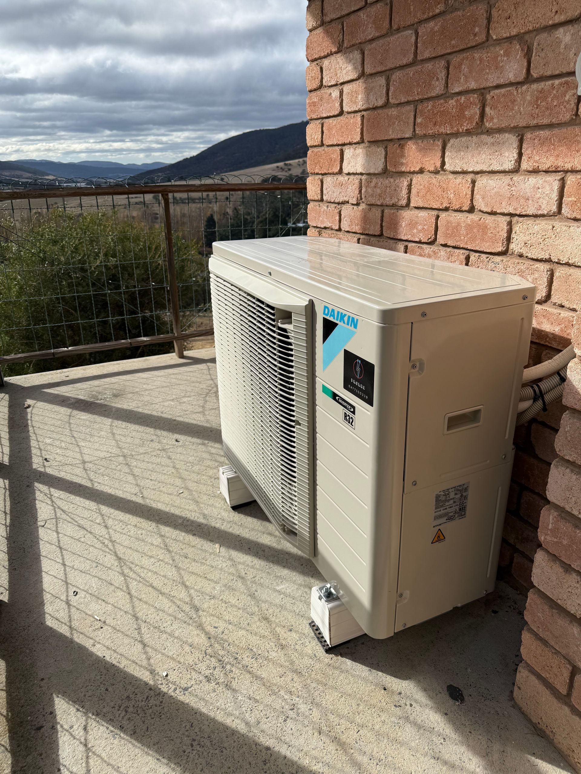 Outdoor heat pump unit beside a brick wall on a sunny patio with mountain view beyond