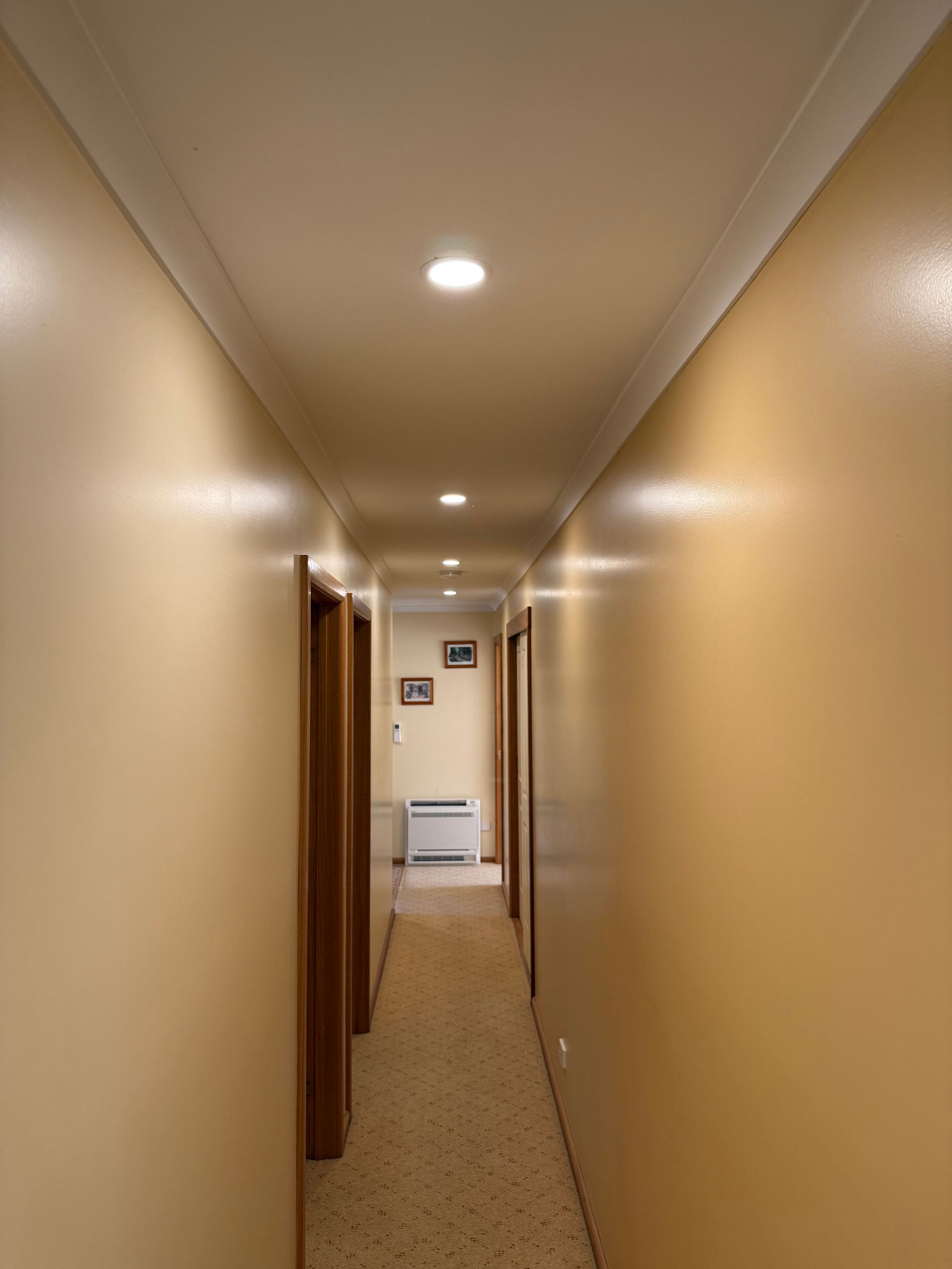 Narrow beige hallway with recessed ceiling lights and a doorway at the far end