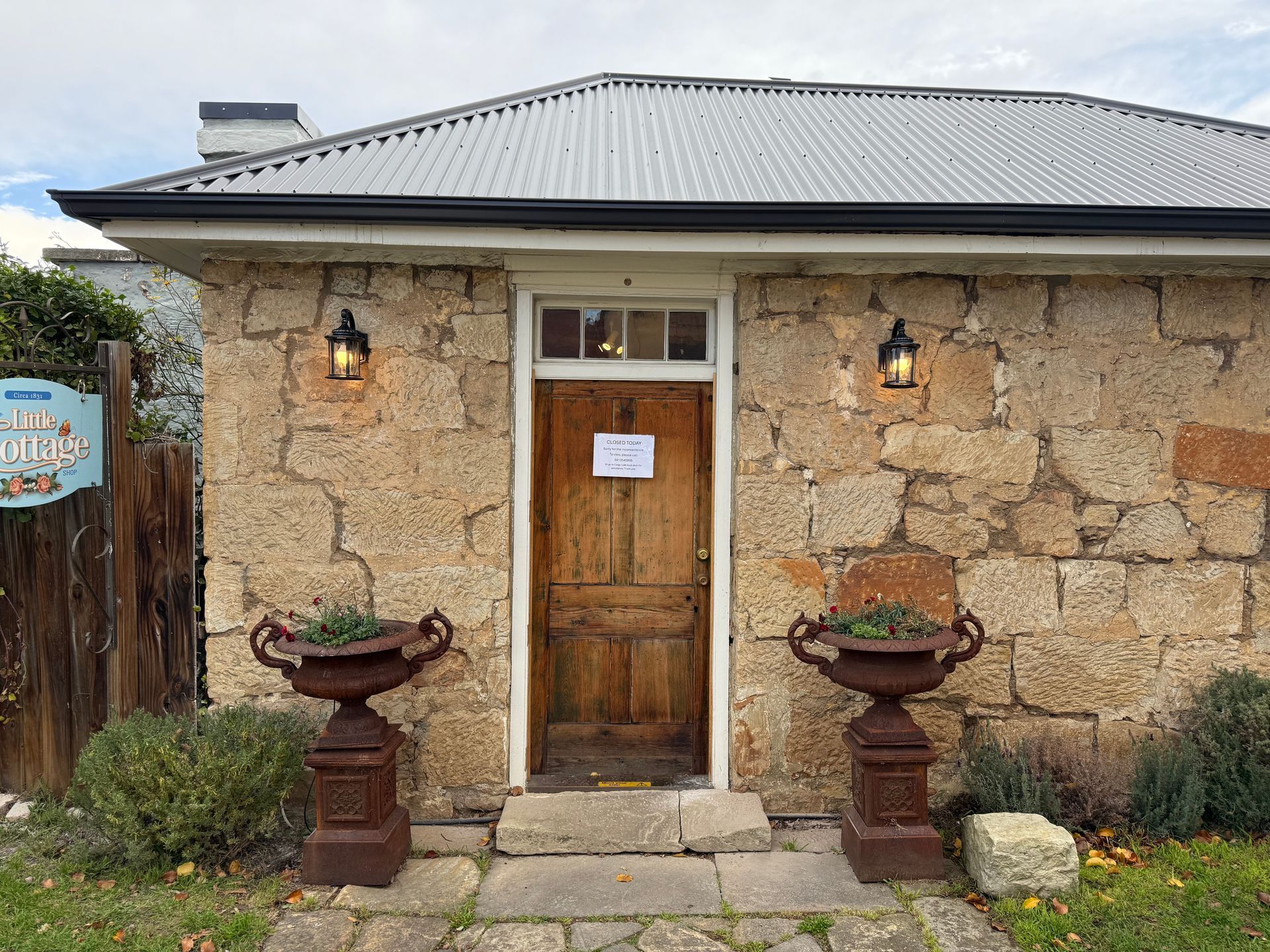 Stone cottage entrance with wooden door, white trim, hanging lanterns, and two potted planters.