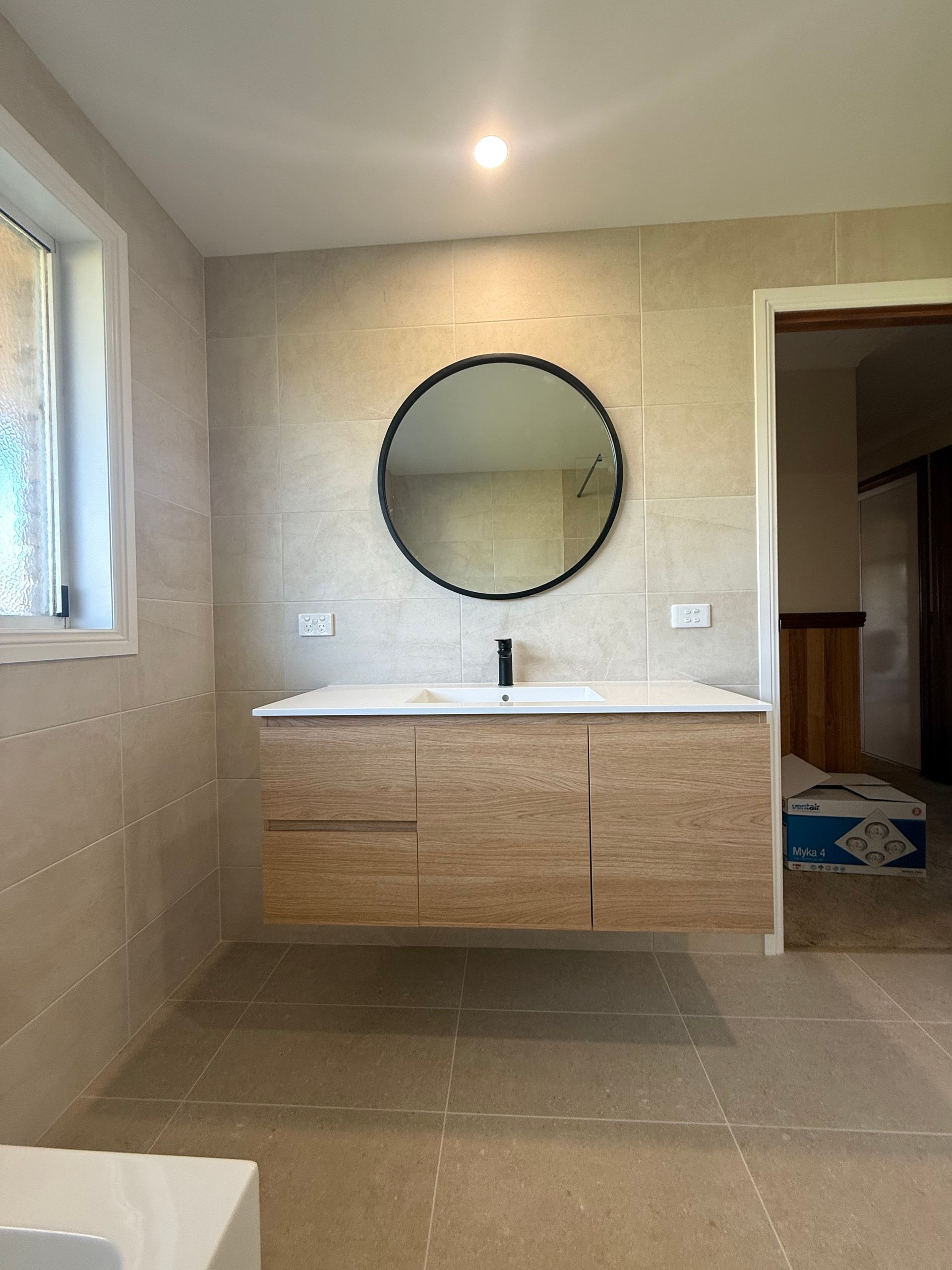 Modern bathroom vanity with round mirror, white sink, wood cabinet, and tiled walls.