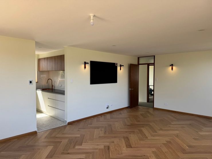 Empty modern living room with herringbone wood floor and open kitchen area