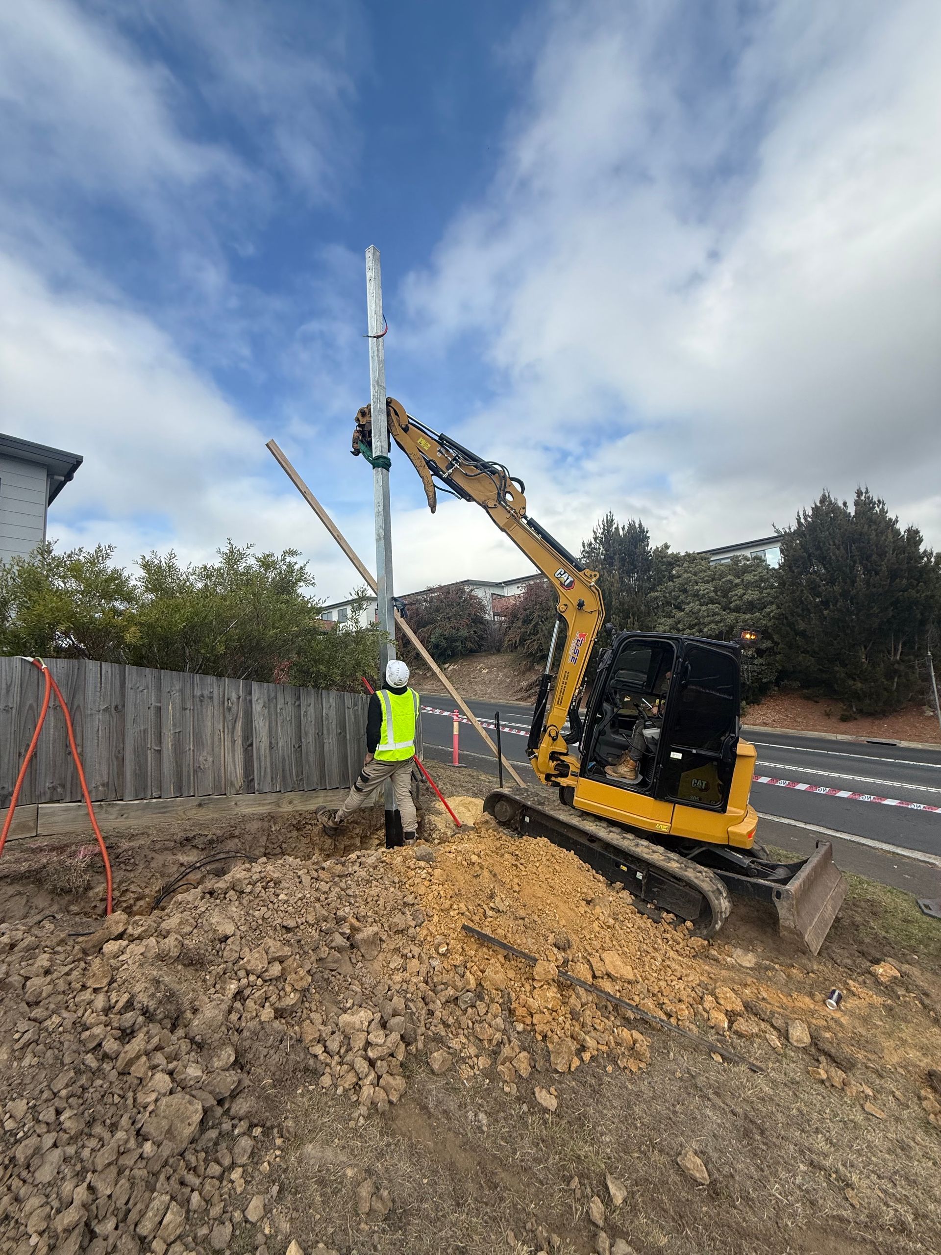 Construction worker beside excavator lifting utility pole on roadside worksite