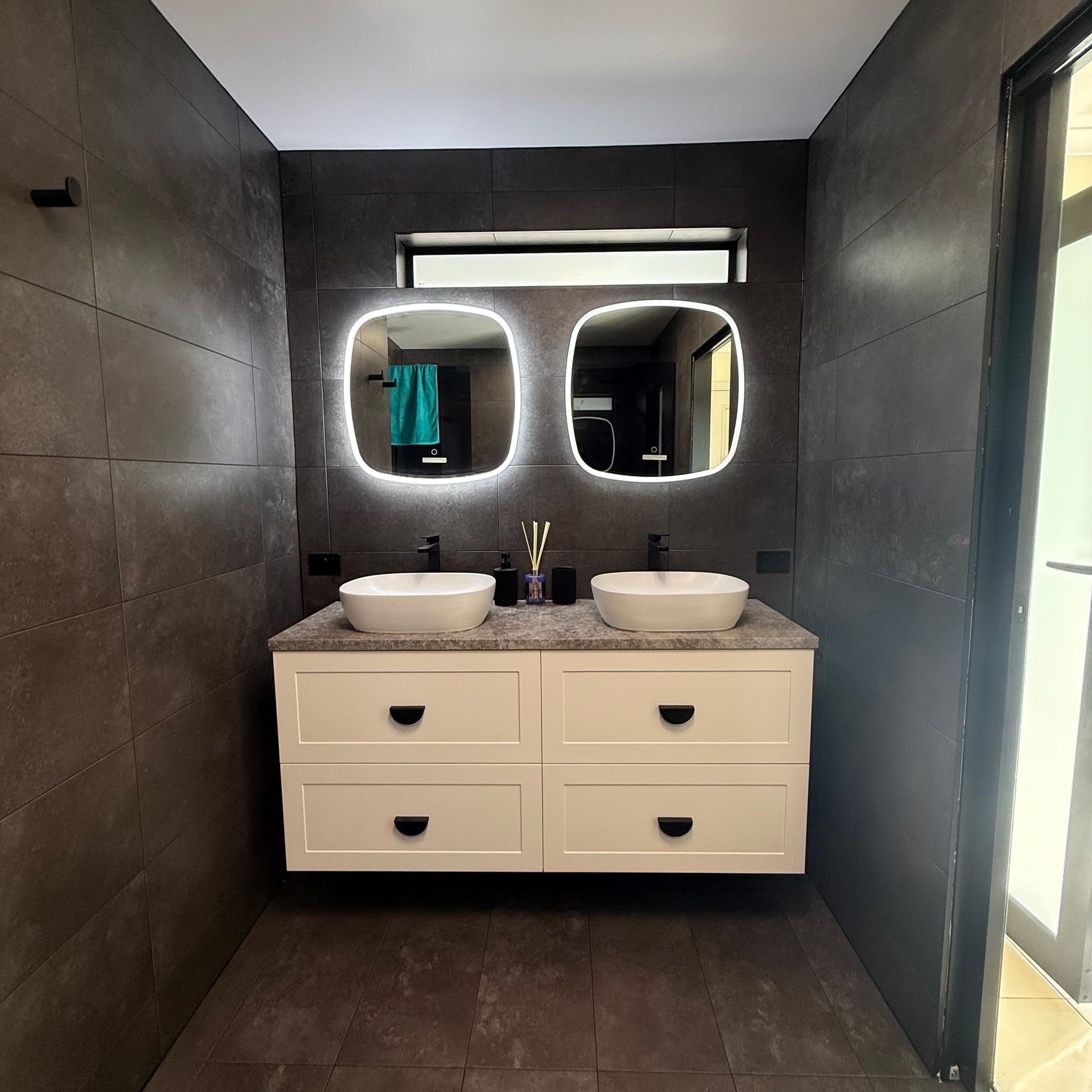 Modern bathroom with double vanity, two round mirrors, and dark tile walls Modern bathroom with double vanity, two round mirrors, and dark tile walls